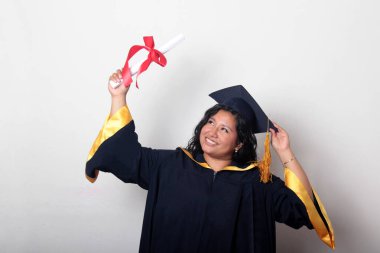 Şapka ve cübbe giymiş genç esmer kadın diplomasını gururla, tatmin olmuş ve kariyerini okulunda bitirmekten mutlu olarak gösteriyor.