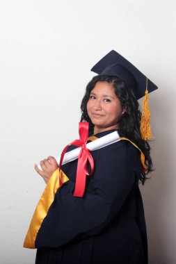 Şapka ve cübbe giymiş genç esmer kadın diplomasını gururla, tatmin olmuş ve kariyerini okulunda bitirmekten mutlu olarak gösteriyor.