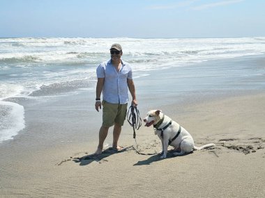 Yetişkin bir adam, plajda terapi olarak beyaz pitbull 'uyla yürüyor ve yanında depresyon ve anksiyeteye karşı beslediği duygusal destek de var.