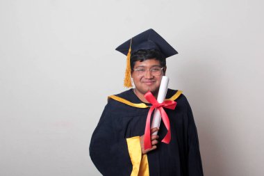 Başlık ve cübbe giyen genç adam gururla diplomasını gösteriyor. Mesleki eğitimini tamamlayıp mezun olmaktan memnun.