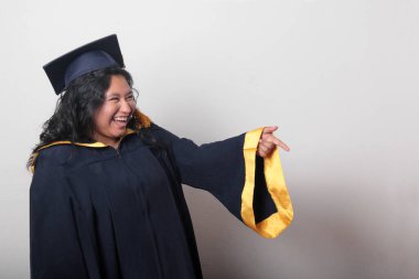 Genç esmer Latin kadın kep ve cübbe giyerek mezuniyetini ve eğitimini tamamlayışını kutluyor.