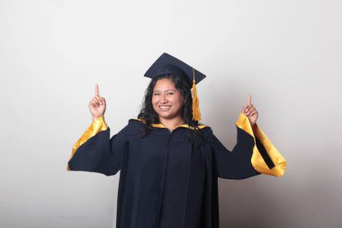 Genç esmer Latin kadın kep ve cübbe giyerek mezuniyetini ve eğitimini tamamlayışını kutluyor.