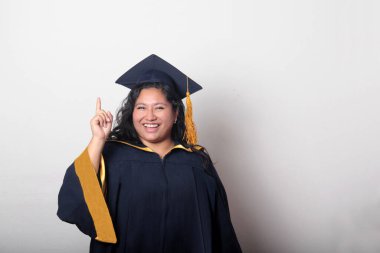 Genç esmer Latin kadın kep ve cübbe giyerek mezuniyetini ve eğitimini tamamlayışını kutluyor.