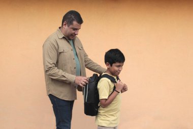 Boşanmış bekar baba, 10 yaşındaki Latin oğluna sırt çantasıyla okula dönmesi için yardım ediyor.