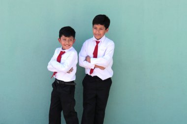 Esmer tenli iki Latin çocuk, ilkokul üniformalı, okula dönmeye hazır, heyecanlı ve mutlu.