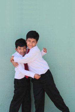Esmer tenli iki Latin çocuk, ilkokul üniformalı, okula dönmeye hazır, heyecanlı ve mutlu.