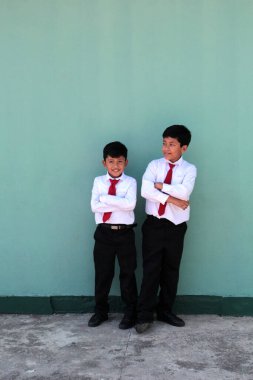 Esmer tenli iki Latin çocuk, ilkokul üniformalı, okula dönmeye hazır, heyecanlı ve mutlu.