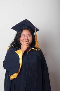 Şapka ve cübbe giymiş genç bir kadın mezuniyet balosunu kutluyor ve düşünceli ve düşünceli görünüyor.