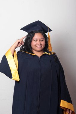 Şapka ve cübbe giymiş genç bir kadın mezuniyetini kutluyor ve düşünceli ve düşünceli görünüyor.