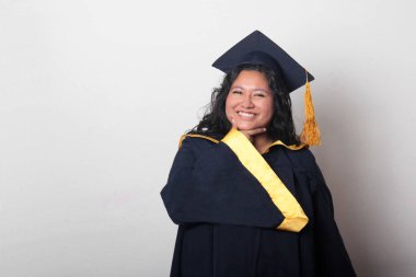 Şapka ve cübbe giymiş genç bir kadın mezuniyetini kutluyor ve düşünceli ve düşünceli görünüyor.