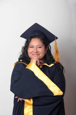 Şapka ve cübbe giymiş genç bir kadın mezuniyetini kutluyor ve düşünceli ve düşünceli görünüyor.