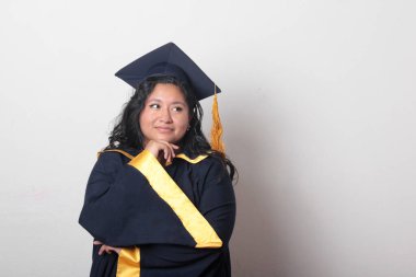 Şapka ve cübbe giymiş genç bir kadın mezuniyetini kutluyor ve düşünceli ve düşünceli görünüyor.