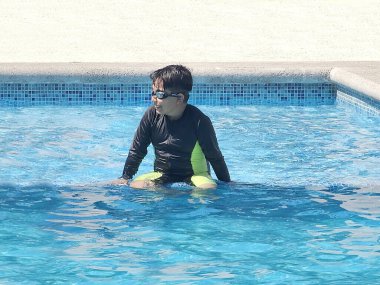 Latin çocuk tatilde ya da hafta sonu havuzda yalnız oynuyor. Kendini güneşten korumak için mayo giyiyor.