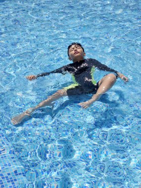 Latin çocuk tatilde ya da hafta sonu havuzda yalnız oynuyor. Kendini güneşten korumak için mayo giyiyor.