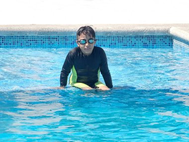 Latin çocuk tatilde ya da hafta sonu havuzda yalnız oynuyor. Kendini güneşten korumak için mayo giyiyor.