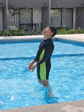 Latin çocuk tatilde ya da hafta sonu havuzda yalnız oynuyor. Kendini güneşten korumak için mayo giyiyor.