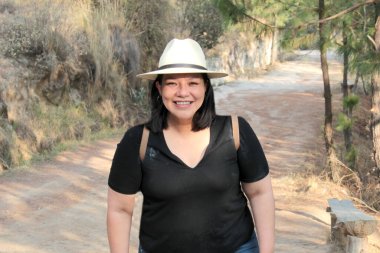 40 yaşındaki Latin bir kadın, doğa ve güneş ışığının tadını çıkarmak için dağlarda yürüyüş yapıyor, refah ve güç kazanıyor.