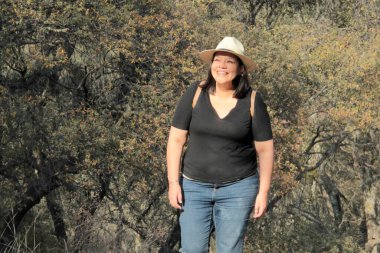 40 yaşındaki Latin bir kadın, doğa ve güneş ışığının tadını çıkarmak için dağlarda yürüyüş yapıyor, refah ve güç kazanıyor.