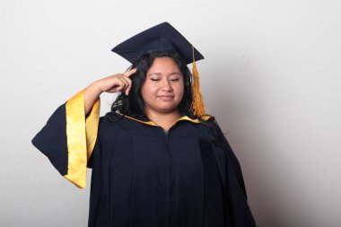 Şapka ve cübbe giymiş genç bir kadın mezuniyet balosunu kutluyor ve düşünceli ve düşünceli görünüyor.