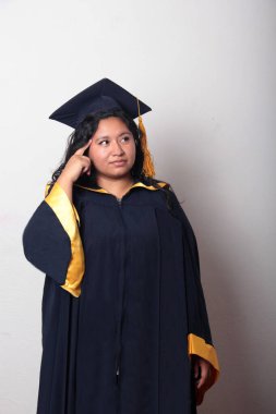 Şapka ve cübbe giymiş genç bir kadın mezuniyet balosunu kutluyor ve düşünceli ve düşünceli görünüyor.