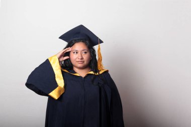 Şapka ve cübbe giymiş genç bir kadın mezuniyet balosunu kutluyor ve düşünceli ve düşünceli görünüyor.