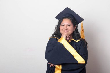 Şapka ve cübbe giymiş genç bir kadın mezuniyet balosunu kutluyor ve düşünceli ve düşünceli görünüyor.