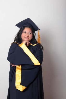 Şapka ve cübbe giymiş genç bir kadın mezuniyet balosunu kutluyor ve düşünceli ve düşünceli görünüyor.