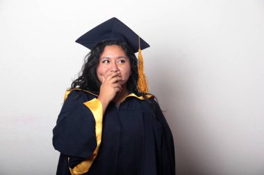 Şapka ve cübbe giymiş genç bir kadın mezuniyet balosunu kutluyor ve düşünceli ve düşünceli görünüyor.