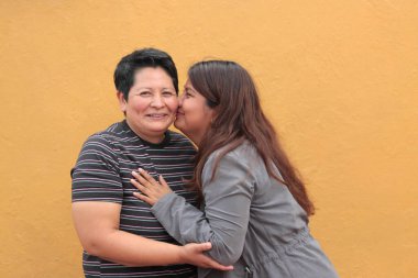 Koyu tenli iki Latin lezbiyen bir çift ve sevgilerini öpücüklerle ve kucaklaşmalarla gösteriyorlar.