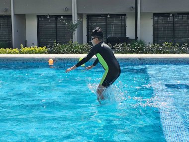 Latin çocuk tatilde ya da hafta sonu havuzda yalnız oynuyor. Kendini güneşten korumak için mayo giyiyor.