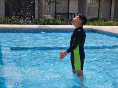 Latin çocuk tatilde ya da hafta sonu havuzda yalnız oynuyor. Kendini güneşten korumak için mayo giyiyor.