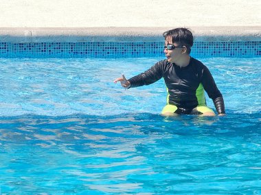 Latin çocuk tatilde ya da hafta sonu havuzda yalnız oynuyor. Kendini güneşten korumak için mayo giyiyor.