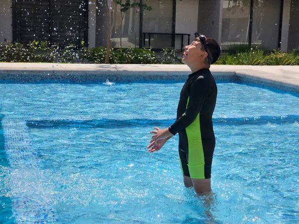 Latin çocuk tatilde ya da hafta sonu havuzda yalnız oynuyor. Kendini güneşten korumak için mayo giyiyor.