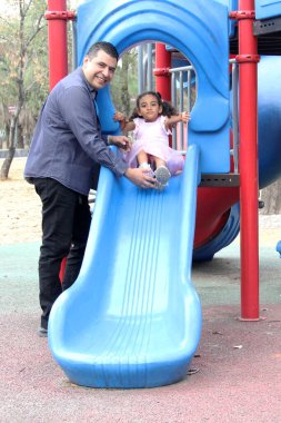 Bekar baba ve 4 yaşındaki kıvırcık saçlı Latin kızı oyun parkında oynuyorlar ve hafta sonu tatillerinde boş vakitlerini geçiriyorlar.