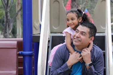 Bekar baba ve 4 yaşındaki kıvırcık saçlı Latin kızı oyun parkında oynuyorlar ve hafta sonu tatillerinde boş vakitlerini geçiriyorlar.