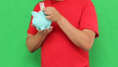 Koyu tenli Latin yetişkin adam domuzcuk kumbarasını gösteriyor, mutlu ve gelecek için biriktirdiği parayı korumak için heyecanlı.