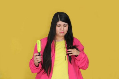 30 yaşındaki Latin kadın, uzun düz saçlarını tarıyor. Hasarlı, susuz ve karışık saçlardan muzdarip.