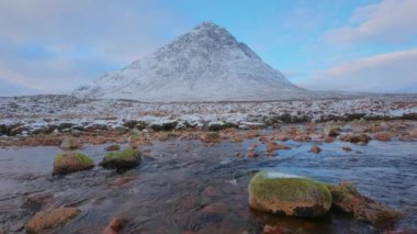 A calm river with stones on the foreground at the foot of a big mountain. Buachaille Etive Mor, the valley of Glencoe, Scottish Highlands, Scotland
