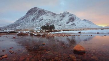 İskoçya, İskoçya 'daki Glencoe Vadisi' nin girişinde Buachaille Etive Mor 'un eteklerinde, ön planda taş olan ücra bir kulübe ve sakin bir nehir.