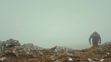 Sırt çantalı bir gezgin sabah bulutlarla kaplı bir dağın tepesine tırmanıyor. Glen Coe, Highlands 'daki Beinn Achrulaiste. İskoçya