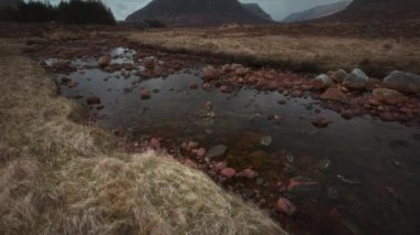 Öndeki Buachaille Dağı Etive Mor ve Rocky Coe Nehri 'nin 4K görüntüleri. 4K video kamera yukarı doğru hareket ediyor. İskoçya İskoçya, İngiltere. 