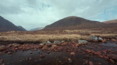 Öndeki Buachaille Dağı Etive Mor ve Rocky Coe Nehri 'nin 4K görüntüleri. Kamera hareketli bir video. İskoçya İskoçya, İngiltere. 