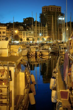 Körfezdeki demirli yatlar gece şehrin arka planında. Savona, Liguria, İtalya, Ağustos 2022