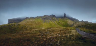 Yüksek keskin uçurumlardan oluşan atmosferik bir manzara, tepeye çıkan yol ve yükselen yağmur bulutu. Storr, Skye Adası, İskoçya, İngiltere