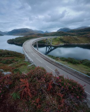 Curved bridge that crosses the lake in autumn. Kylesku Bridge crossing the Loch a Chairn Bhain in Sutherland, on the North Coast 500, Scotland clipart