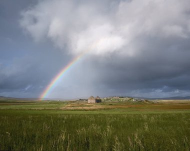 Tarlada eski bir mezarlık ve gökkuşaklı yağmur bulutları. Kilmuir Mezarlığı. Kuzey Uist, Outer Hebrides, İskoçya