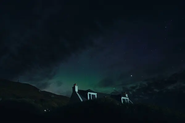 Kuzey Işıkları ve yalnız bir ev boyunca yıldızlı gökyüzü. Skye Adası, İskoçya 