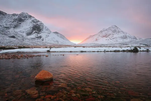 Calm river with stone on the foreground at the foot of Buachaille Etive Mor at the entrance to the valley of Glencoe in the Scottish Highlands, Scotland
