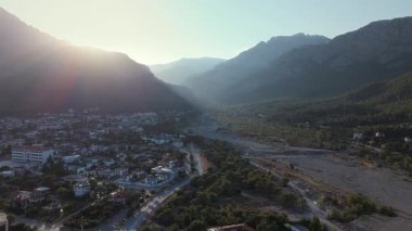 Gün batımında dağ vadisi ve şehrin hava aracı görüntüsü. Dağların ve şehir manzarasının üzerinde akşam güneşi. Goynuk, Türkiye