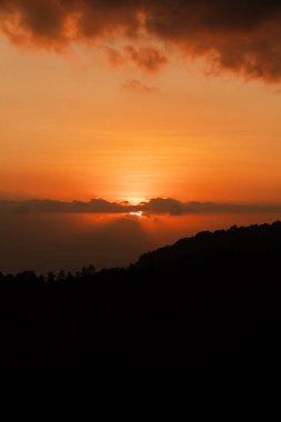 Bulutların ve siluetli tepelerin ardında gün batımı